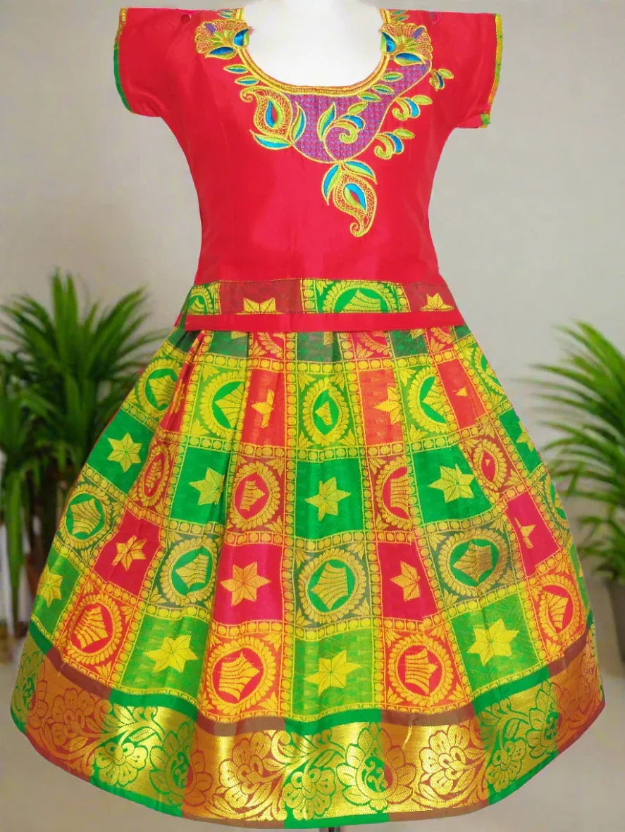 A traditional Pattu Pavadai set for girls featuring a red silk blouse with gold and multicolor embroidery and a multicolor silk skirt with a golden zari border.