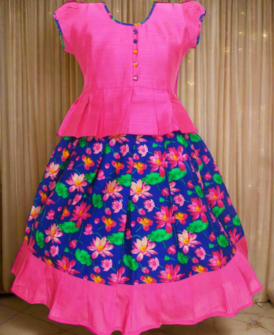Girls Kalamkari cotton Pattu Pavadai with Blue floral skirt and Pink ruffle border, paired with a Pink peplum blouse enhanced with Potli buttons.