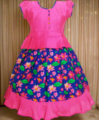 Girls Kalamkari cotton Pattu Pavadai with Blue floral skirt and Pink ruffle border, paired with a Pink peplum blouse enhanced with Potli buttons.