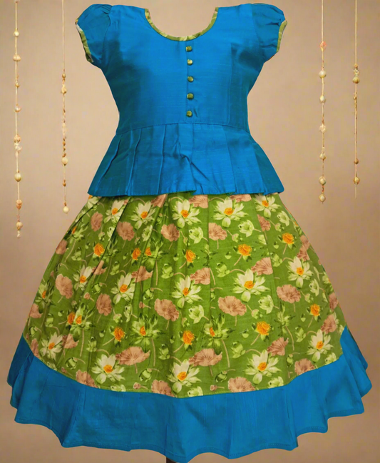 Girls Kalamkari cotton Pattu Pavadai with Parrot green floral skirt and Turquise ruffle border, paired with a Turquise peplum blouse enhanced with Potli buttons.